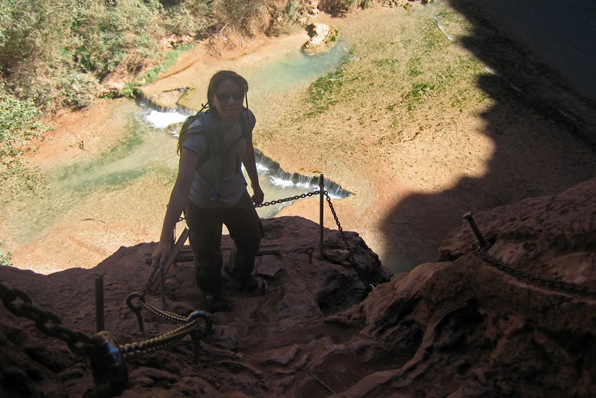 Here's Niki on the landing just before she starts the climb down.  Mooney Falls is 200' tall, which makes it about 30' taller than Niagara Falls.  The tunnels we have just passed through were enlarged from natural caves around 1882.  It was then that a prospector named D.W. Mooney fell to his death here while his party was trying to find a way to get below the falls.  His body remained below for eleven months before a local Indian showed the miners the natural caves which they then enlarged and then proceeded to sink metal rods in the cliff face to aide in the descent.  Mooney was then buried near the falls.  Just something to think about while climbing!