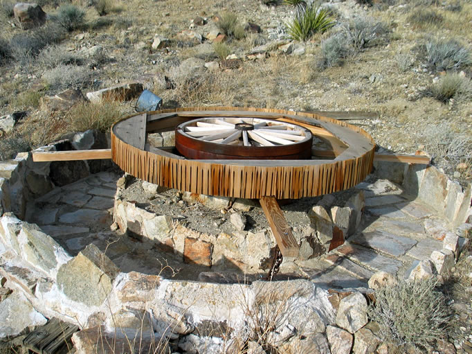 A small four horsepower International upright gas engine drove the wagon wheel through a pulley.  Ore would be placed in the rock lined channel and as the wheel turned it would pull heavy drag stones over the ore, crushing it.