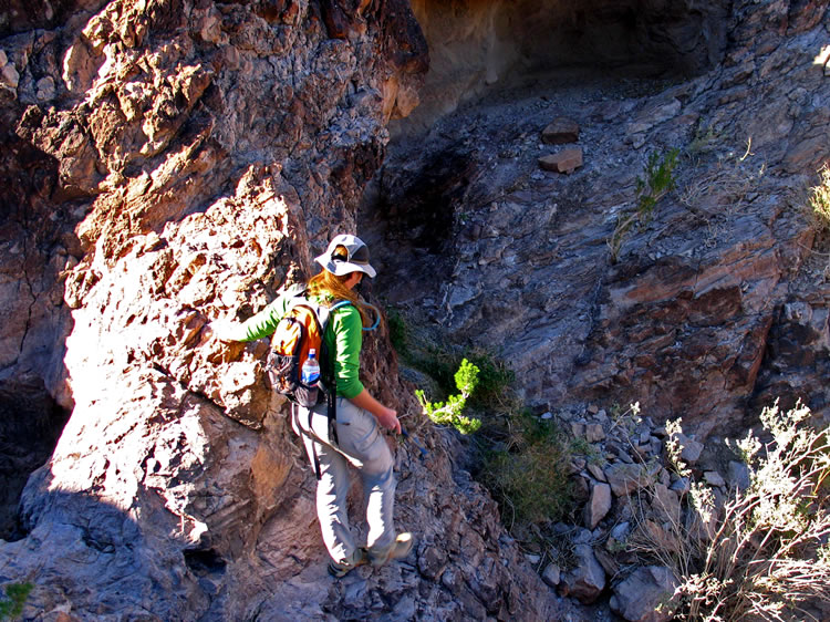 Soon the canyon bottom narrows and is crossed by rock dikes.  There is a deep, moderately sized natural tank here.  During a rainstorm the stream would fill the tank before plunging as a waterfall to the canyon bottom.  Niki is crossing the face of the dry waterfall to get to a small shelter on the other side of the canyon.