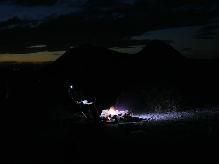 We set up camp by the light from our headlamps and relax in front of a crackling fire.  The lights in the distance are back toward Cadiz and Amboy,  some ten miles away.
