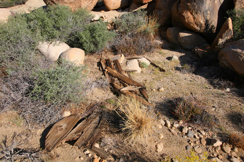 In front of the stacked stones is a scatter of old wood and cans.